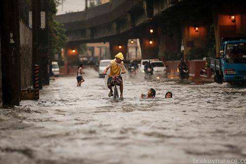 Филипинец на велосипед минува покрај деца што си играат во поплавената улица во Манила