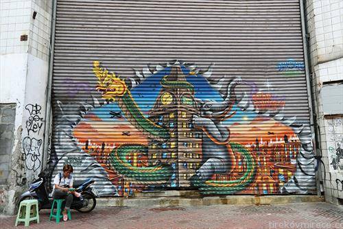 чита од својот мобилен телефон додека седи до еден графит на портите од напуштениот трговски центар во популарната туристичка област во Банкок
