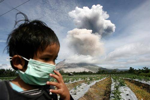 Дете од Индонезија носи маска за да си го покрие лицето како заштита од пепелта која извира од вулканот на планината Синабунг, во Северна Суматра.
